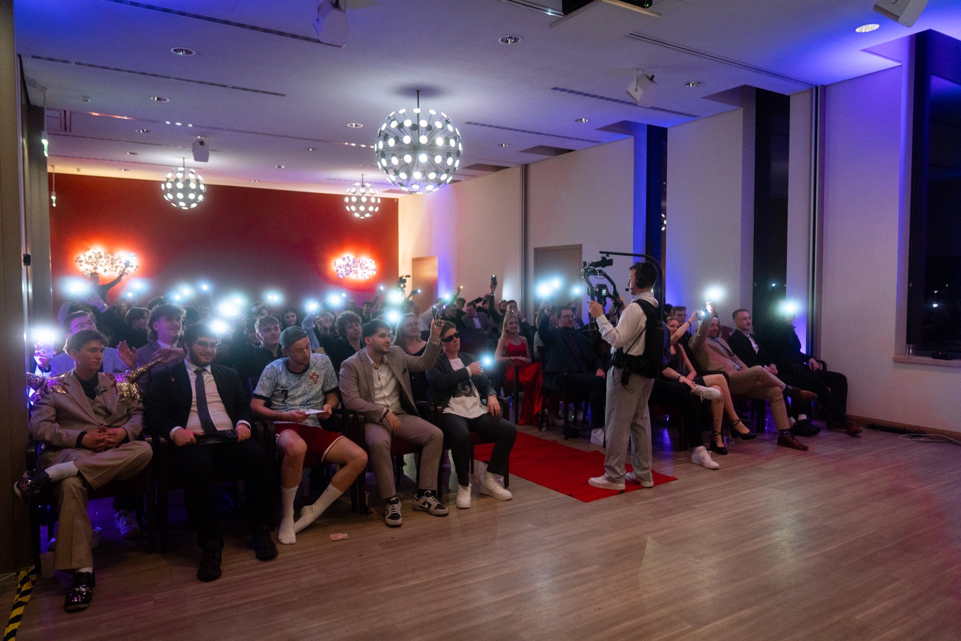 Publikum im Saal hält leuchtende Handylichter hoch, vorne filmt ein Kameramann