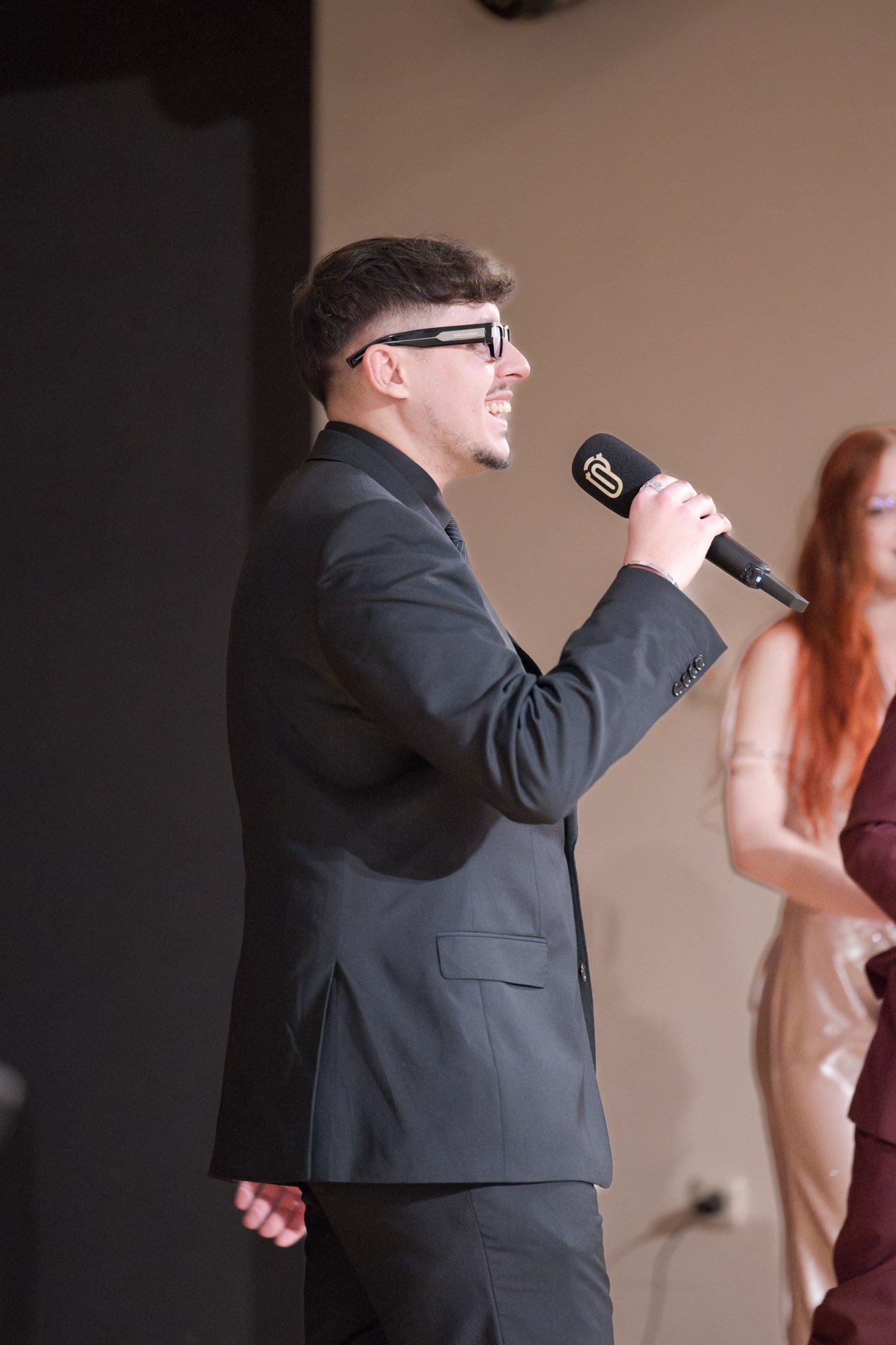 Ein Act im dunklen Anzug singt in das Mikrofon mit Clip-Awards-Emblem