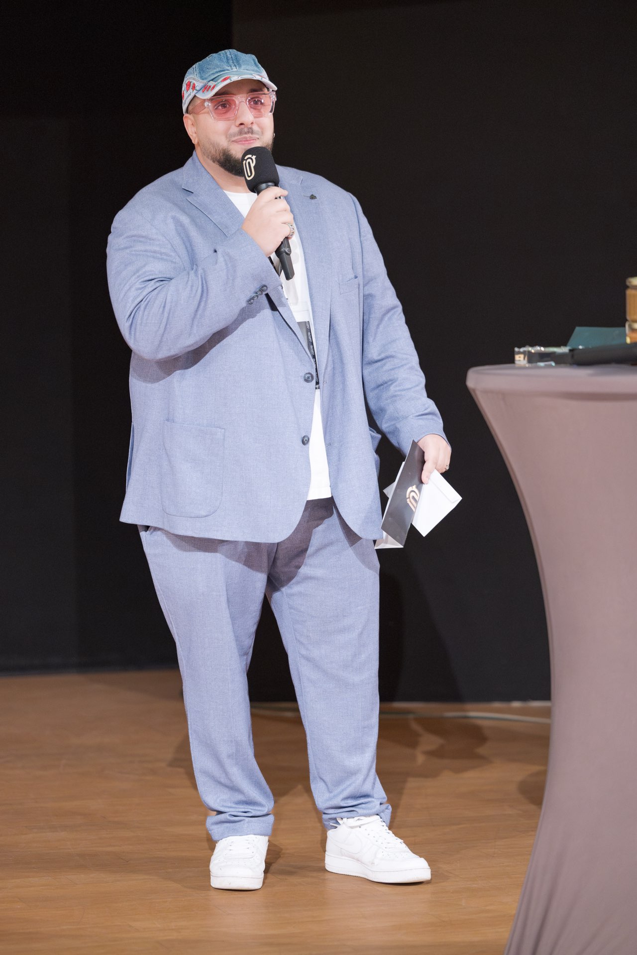 Moderator mit Mikrofon und Karten am Stehtisch auf der Bühne